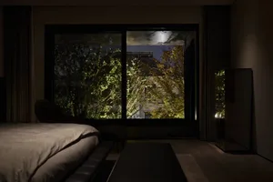 A modern bedroom featuring glass walls with a view of the outdoors at dusk.