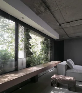 A modern industrial living room featuring concrete and glass materials with green plants.
