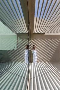 A modern interior space with glass walls and concrete elements, featuring diagonal light patterns.