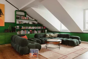 A modern living room featuring a green fabric sofa, a round glass-top coffee table, and a bookshelf filled with books and dec