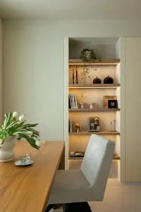 A minimalist home office with a wooden desk, a grey chair, and built-in shelves with decorative items.