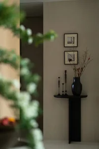 A minimalist interior space featuring a black metal console table with decorative branches and candle holders.