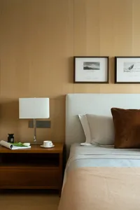 A contemporary bedroom featuring a white upholstered bed with a wooden bedside table, light-colored walls, and framed art on 