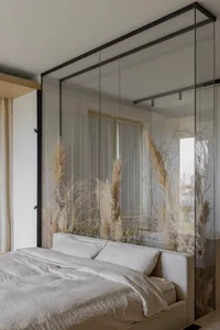 Bedroom featuring a bed with white bedding and pampas grass, behind a glass partition.