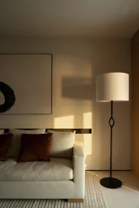 A minimalist living room with a couch, cushions, a standing lamp, and a large framed wall art.