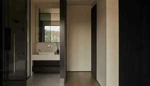 Modern bathroom with a glass countertop and sink, visible through a glass door leading to another room. Light wood flooring a