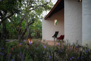 Outdoor patio with concrete floor, chairs, and a fire pit surrounded by greenery and flowers.