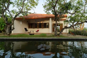 Traditional village house with red tiled roof, white walls, and brick exterior by a calm water body.