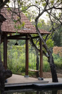 A wooden structure with a tiled roof and a hanging swing, surrounded by greenery and trees.