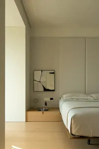 A minimalist bedroom with a white bed and floating nightstand, featuring modern lighting and clean lines.