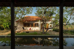 A minimalist residential home constructed of sandstone, surrounded by lush greenery and a tranquil pool.