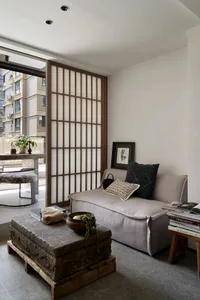 A modern living room featuring a concrete coffee table on wooden pallets, a minimalist sofa with cushions, and a wooden scree