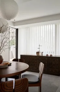 Modern dining room with round wooden table, black chairs, wooden cabinet, and white sheer curtains.