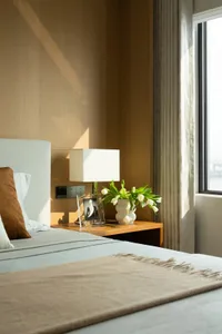 A modern minimalist bedroom featuring a wooden bed frame, fabric bedding, and a glass lamp and vase with white tulips.