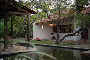 A cozy cottage nestled by a pond with natural stone walls and wooden accents.