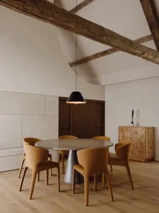 Industrial dining room with concrete table, wooden chairs, and rustic ceiling beams