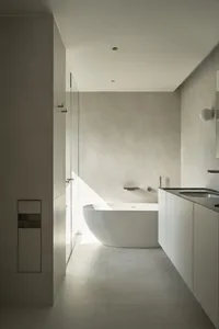 A minimalist bathroom with an open concept design, featuring a modern bathtub, a wall-mounted sink, and a glass shower door.