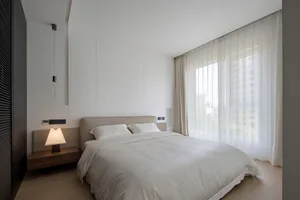 A minimalist bedroom with a neatly made bed, white sheets, and a hanging light bulb.