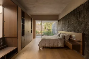 Minimalist bedroom featuring hardwood flooring and a stone wall.