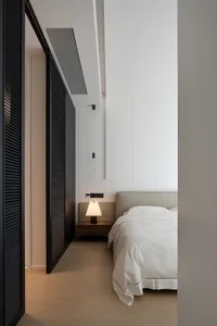 Minimalist bedroom with a wooden floor, white bedding, and a lamp on the bedside table.