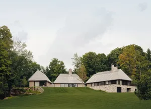 A modern, stone-roofed house surrounded by greenery, with a spacious lawn and trees in the background.
