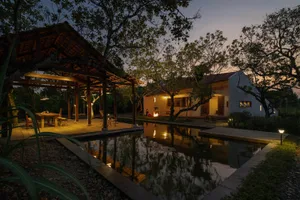Modern house exterior with wooden pergola, brick walls, stone patio, and water feature during evening time.