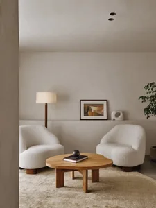 A modern living room with a white sofa, round wooden table, and abstract wall art.