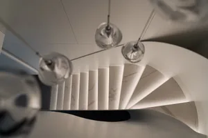A modern staircase with white marble steps and a white marble wall, viewed from above with three hanging light fixtures.
