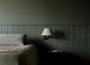 A minimalist bedroom with wooden walls and a comfortable bed, featuring a simple bedside lamp and a small table.