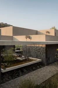 Modern minimalist house exterior with concrete walls and a stone wall with a koi pond and garden area.