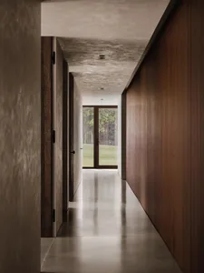 A modern minimalist hallway with concrete flooring and walls, featuring wooden doors and a glass door leading to a green outd