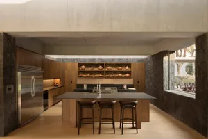 A modern residential kitchen featuring wooden cabinets and a concrete countertop with a bar stool seating area.