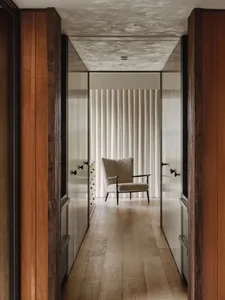 A minimalist corridor with wooden flooring and a single white chair at the end, framed by wooden walls.
