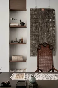 Minimalist office with wooden shelves, paper artwork, and a wicker-back chair.
