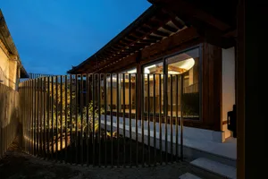 A modern building with wooden exterior at dusk, with illuminated interior visible through large windows.