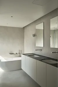 A modern minimalist bathroom featuring a freestanding bathtub made of white marble and a white vanity with black marble count