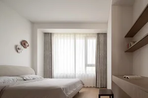 A modern bedroom with fabric headboard, wooden sides of the bed and floating desk on the wall, featuring sheer curtains over 