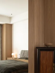 A modern bedroom with a wooden headboard and nightstand, featuring a gray bedspread and a small table lamp next to the bed.