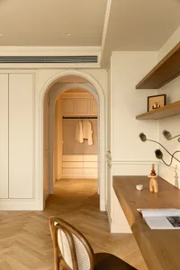 A modern home office with an archway entrance to a closet featuring wooden furniture and architectural molding.