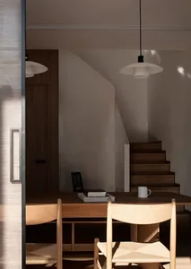 Modern home office featuring wood furniture, books, and a white mug under a pendant light.