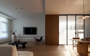 A modern minimalist apartment featuring wooden floors, glass sliding doors, and concrete walls.