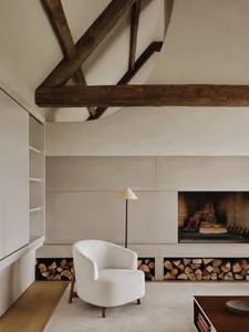 Modern minimalist living room with concrete walls, a white armchair, and a fireplace with firewood storage.
