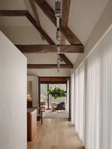 A modern minimalist living room with wooden beams, white curtains, and a green potted plant.