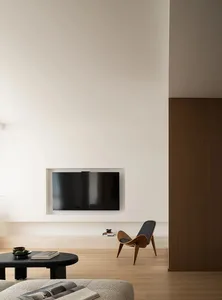 Modern minimalist living room with a sleek black television embedded in the wall, a wooden shell chair, and a black ottoman w