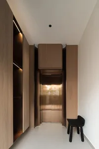 A minimalist walk-in closet with wooden cabinets, glass doors, and ledges, featuring a sleek black chair.