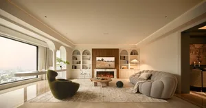 A modern, neutral-tones living room interior with a fireplace, bookshelves, and a comfortable seating area.
