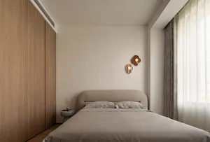 A minimalist bedroom featuring a bed with a neutral-colored headboard and bedspread, along with a simple nightstand and decor