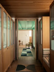 A minimalist residential corridor features wooden walls, floors, and cabinets, with a green-painted ceiling and a patterned r
