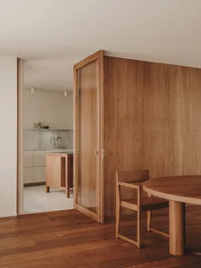 A modern dining space with wooden furniture and a kitchen area in the background.