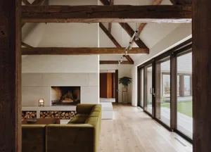 Modern living room with wood beams, plaster walls, and floor-to-ceiling windows.